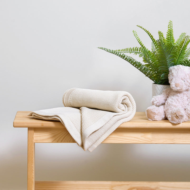 Cream Organic Knitted Baby Blanket rolled on an oak table in a beige nursery | Cosy Baby Blankets & Swaddles | Nursery Bedding | Newborn Baby Essentials - Clair de Lune UK