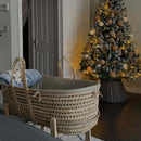 sage Organic Palm Moses Basket on Pine Rocking Stand next to a gorgeous snow-covered Christmas tree with cream and brown decorations. | Moses Baby Baskets & Bassinets | Nursery Furniture - Clair de Lune UK