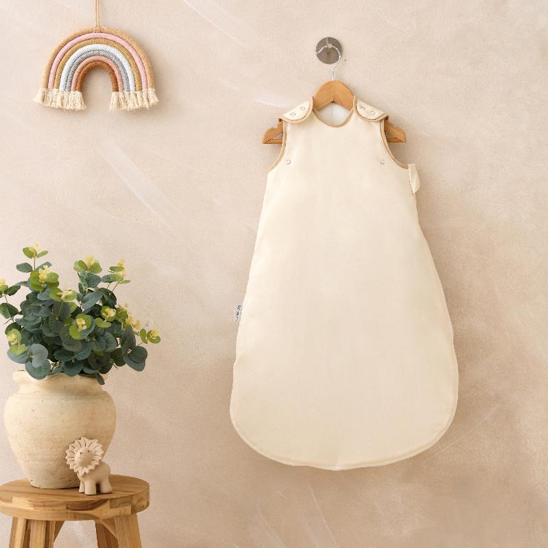 Cream Organic Sleeping Bag hanging on the wall of the nursery next to a vase of flowers | Baby Sleep Accessories | Swaddles - Clair de Lune UK