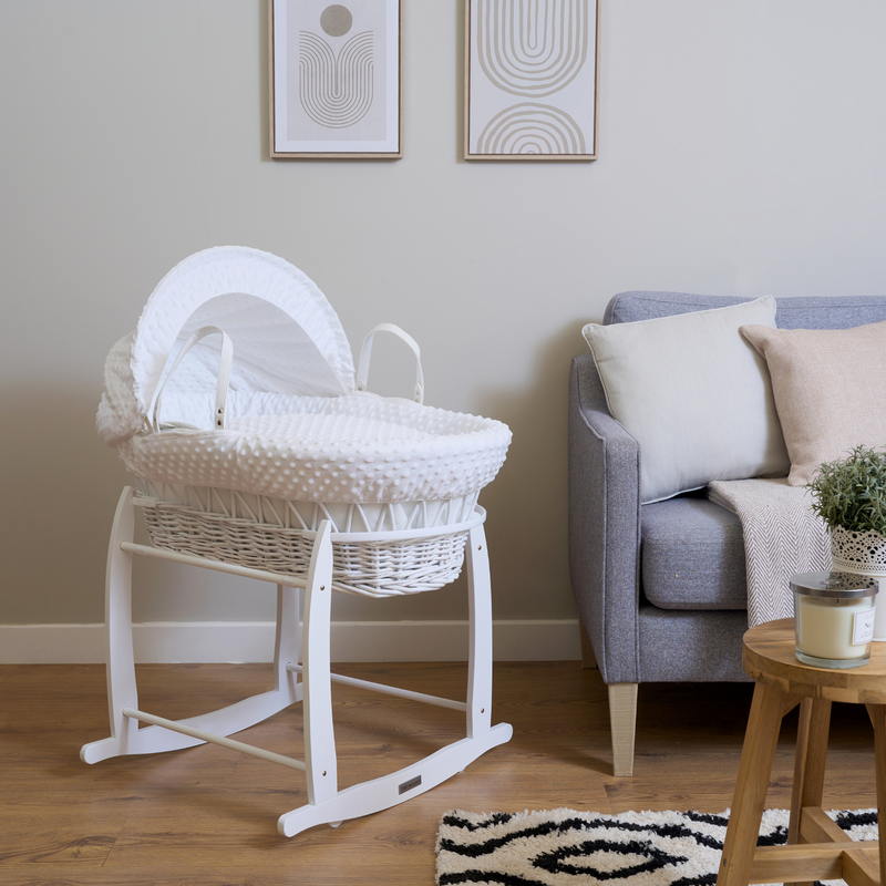 White Dimple White Wicker Moses Basket on a White Deluxe Rocking Stand in next to a grey sofa in a beige living room| Moses Basket Stand | Moses Baby Baskets & Bassinet Accessories | Nursery Furniture - Clair de Lune UK