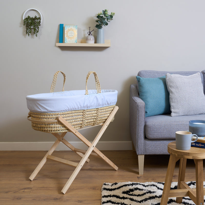 Blue Stripe Palm Moses Basket on Natural Folding Stand in Living Room next to grey sofa | Bassinets | Nursery Furniture - Clair de Lune UK