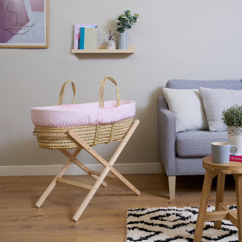 Pink Stripe Palm Moses Basket on Natural Folding Stand in living room next to a grey sofa | Bassinets | Nursery Furniture - Clair de Lune UK