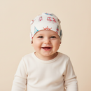 A smiling baby wearing the GrowGrows Seaside Sailor Baby Hat featuring watercolour lighthouse, boats and lifesavers | Bamboo Babywear  Clair de Lune UK
