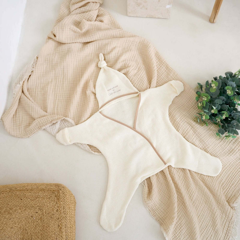  Cream Organic Star Breathable Mesh Baby Wrap Blanket laid out flat on the floor next to soft muslins and plants | Cosy Baby Blankets and Swaddles | Newborn Summer Essentials - Clair de Lune UK
