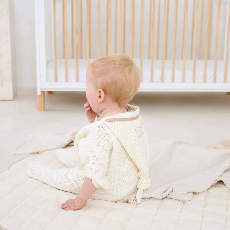 Baby Wearing the Cream Organic Star Breathable Mesh Baby Wrap Blanket while sat on the floor of the beige nursery | Cosy Baby Blankets and Swaddles | Newborn Summer Essentials - Clair de Lune UK