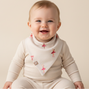 A smiling baby wearing a cream ribbed long-sleeve outfit and a matching cream GrowGrows Tiny Twirls Bib with pink ballerina prints, posed against a warm beige studio background. | Bamboo Babywear - Clair de Lune UK