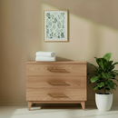 Wooden dresser with 2 pack fitted bedside crib sheets and a plant against a beige wall with a framed picture. | Soft Baby Sheets | Bedside Crib bedding - Clair de Lune UK