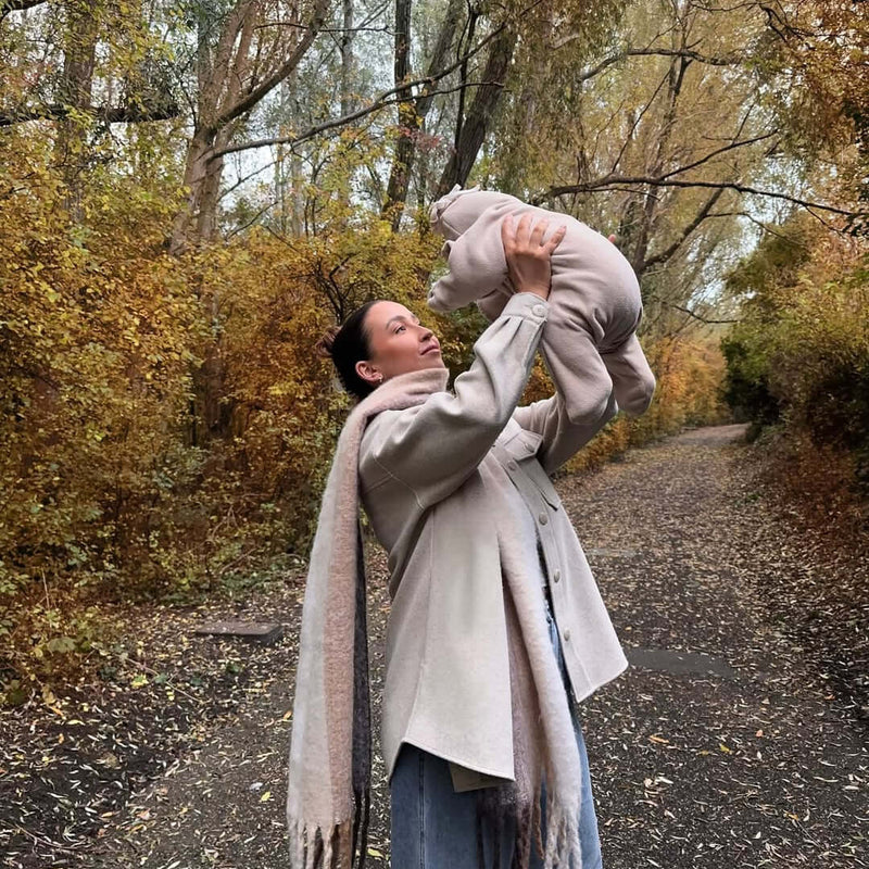 Mum holding baby wearing the oatmeal brown star fleece baby wrap blanket while on an autumn walk in the woods | Baby Blankets and Swaddles - Clair de Lune UK