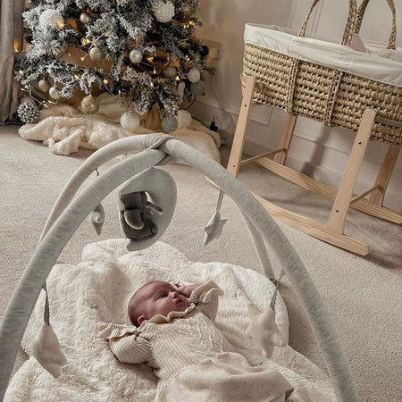 Newborn baby dressed in Christmas outfit lying beside a snowy Christmas tree by the Scandi Palm Moses Basket in Rocking Stand | Moses Baby Baskets & Bassinets | Nursery Furniture - Clair de Lune UK