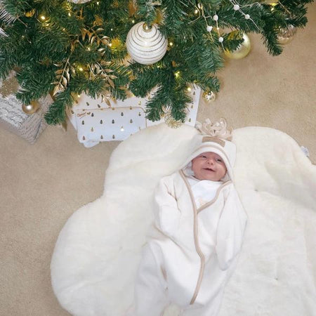 Newborn baby wrapped up snug in their cream Star Fleece Wrap blanket.  Smiling for the camera under the Christmas tree | Baby Blankets and Swaddles | Nursery Linen - Clair de Lune UK