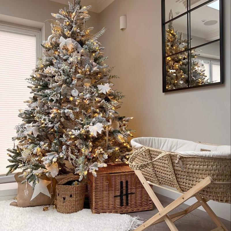 Cream Organic Palm Moses Basket on Pine Folding Stand next to a gorgeous snow-covered Christmas tree with cream and white decorations. Hampers, gifts and  presents under the tree | Moses Baby Baskets & Bassinets | Nursery Furniture - Clair de Lune UK