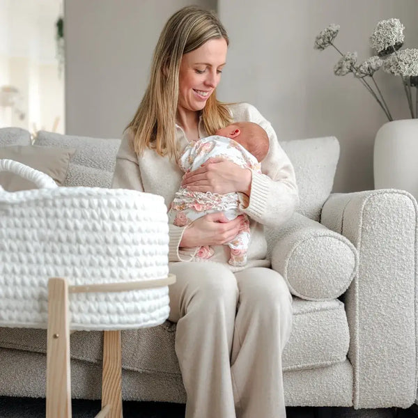 Mum holding her newborn baby next to the White Crochet Moses Basket With Stand in a neutral a white living room | Moses Baby Baskets & Bassinets - Clair de Lune UK