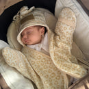 A baby sleeping in a brown carry cot wrapped in a cream and tan Leopard Star Fleece Baby Wrap Blanket, set against a background of fallen yellow autumn leaves. | Cosy Baby Blankets | Pram Blanket - Clair de Lune UK 