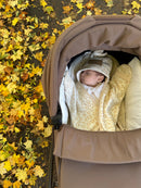 A baby sleeping in a brown stroller wrapped in a cream and tan Leopard Star Fleece Baby Wrap Blanket, set against a background of fallen yellow autumn leaves. | Cosy Baby Blankets | Pram Blanket - Clair de Lune UK 
