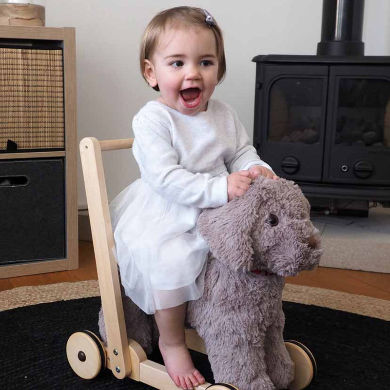 Toddler girl is laughing happily while riding on the Little Bird Told Me Bailey Dog Push Along, Baby Walker and Ride On | Montessori Activities For Babies & Kids | Toys | Baby Shower, Birthday & Christmas Gifts - Clair de Lune UK