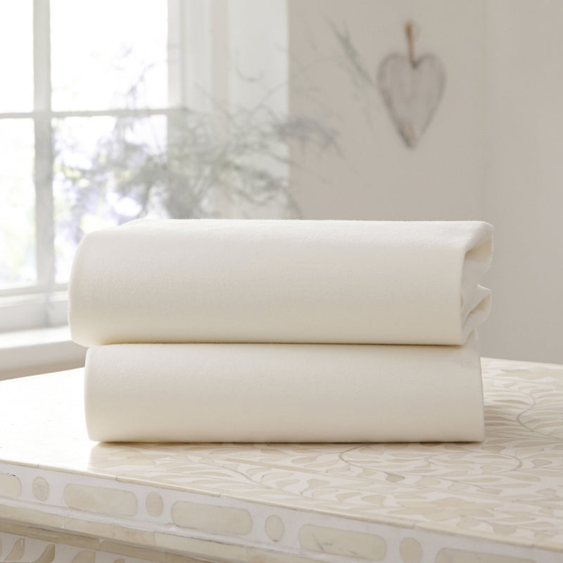 A Pack of 2 Folded Cream Fitted Cotton Moses Fitted Sheets - 74 x 30 cm on the countertop | Soft Baby Sheets | Cot, Cot Bed, Pram, Crib & Moses Basket Bedding - Clair de Lune UK